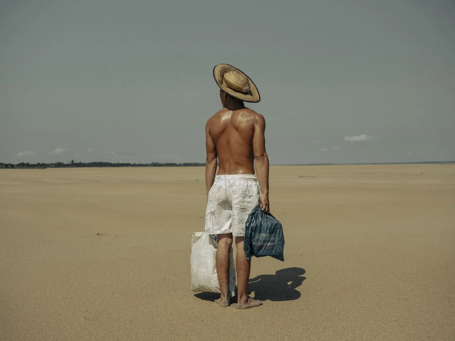 A young man brings food to his mother who lives in the village of Manacapuru. The village was once accessible by boat, but because of the drought, he must walk 2 kilometers along the dry riverbed of the Solimões River to reach her. Amazonas, Brazil,