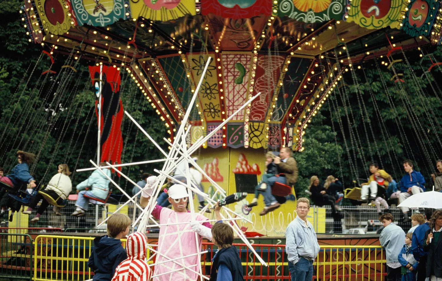A performer entertains visitors in front of Kenny Scharf’s painted chair swing ride. Luna Luna, Hamburg, Germany, 1987