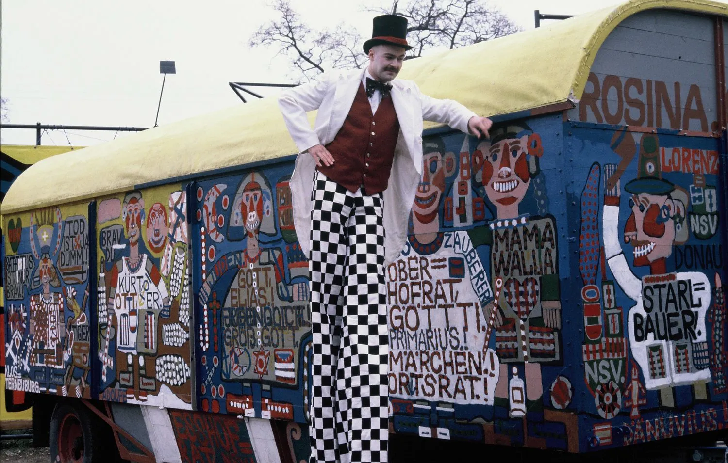 Performer in front of August Walla’s painted circus wagon